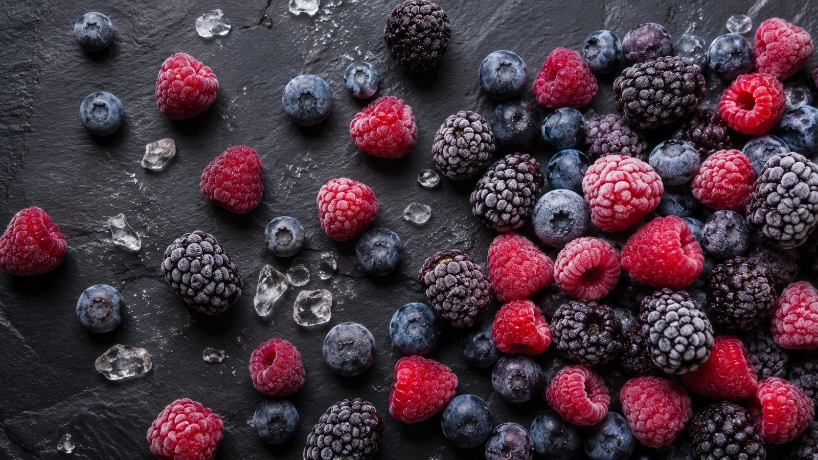 A variety of premium frozen berries including blueberries and raspberries on a dark surface.