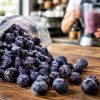 Frozen blueberries spilling onto a cafe counter with a smoothie being prepared
